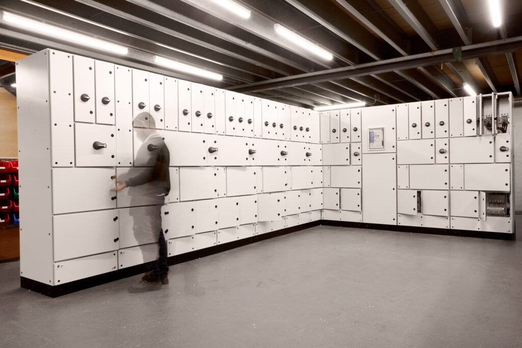 A large room filled with modular electrical switchgear panels, with a technician inspecting one of the units.
